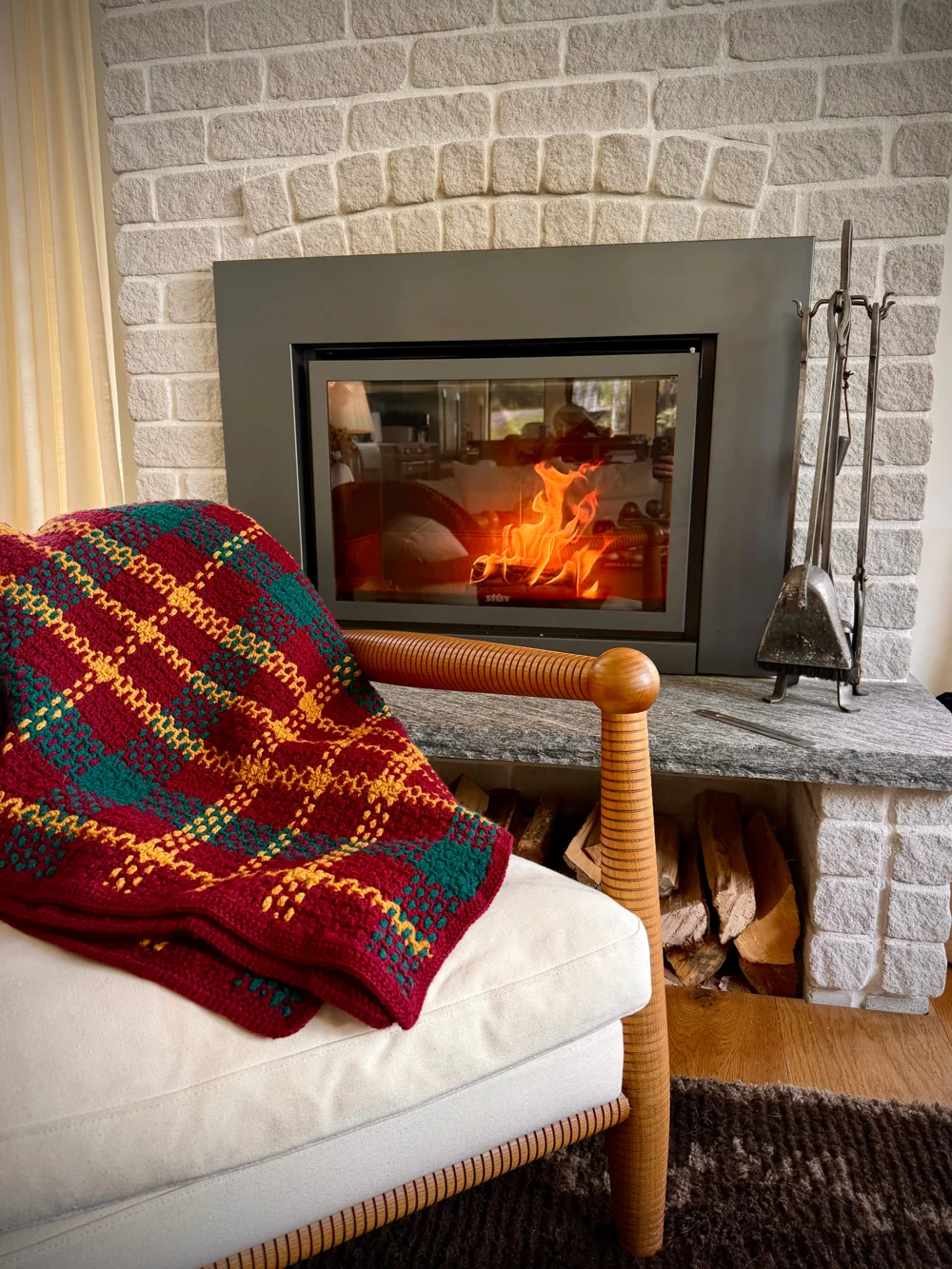 Burgundy, teal and gold tartan crochet blanket beside a fireplace